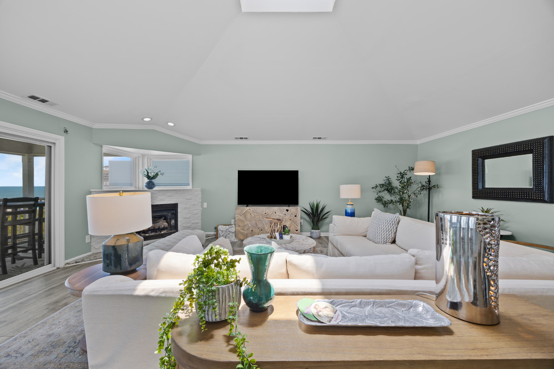 The main living room with deep sofas facing the fireplace and the ocean door beyond